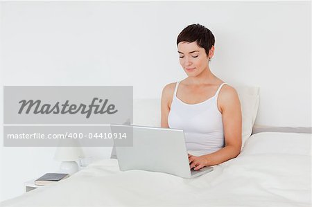 Charming brunette using a laptop in her bedroom