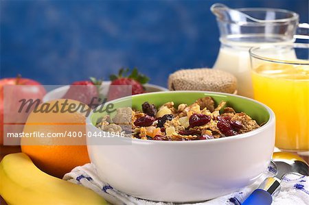Delicious healthy breakfast with a bowl full of wholewheat flakes mixed with dried fruits (cranberries, bananas, raisins and some others) and nuts with fresh fruits, yogurt, milk and orange juice around (Selective Focus, Focus one third into the bowl)