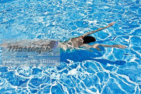 Young man swimming under blue water in swimming pool