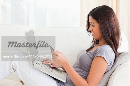 brunette woman working on notebook with card in hands while in the livingroom