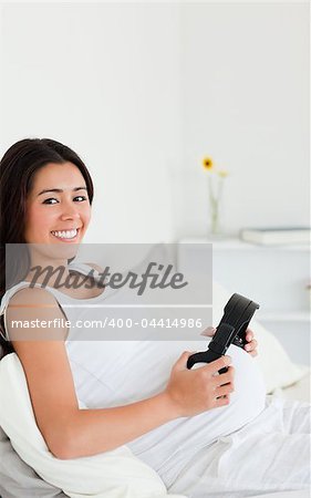 Attractive pregnant woman putting headphones on her belly while lying on a bed at home