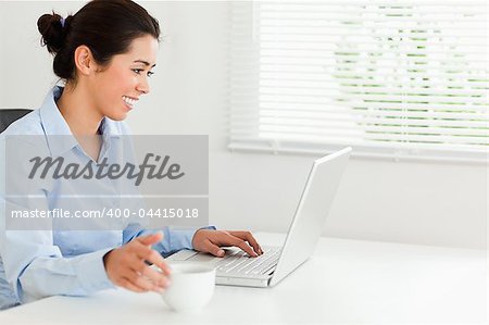 Charming woman relaxing with her laptop while enjoying a cup of coffee at the office