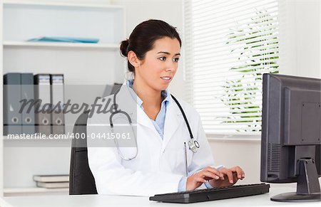 Gorgeous female doctor typing on a keyboard while sitting in her office