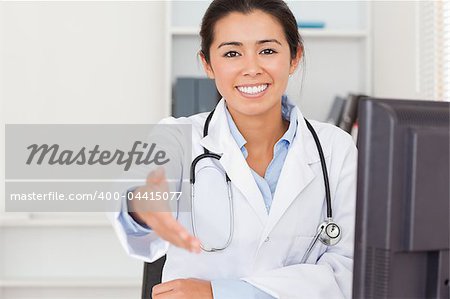 Attractive female doctor inviting somebody to seat while looking at the camera in her office