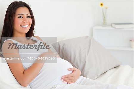 Cute pregnant woman touching her belly while lying on a bed at home