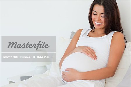 Gorgeous pregnant woman posing while lying on a bed at home