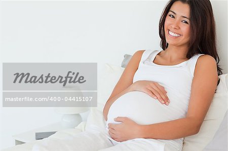 Beautiful pregnant woman posing while lying on a bed at home