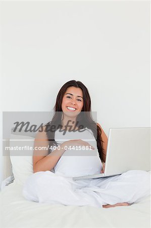 Good looking pregnant woman relaxing with her laptop while lying on a bed at home