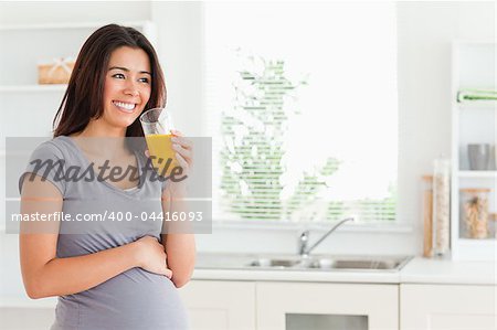 Good looking pregnant woman drinking a glass of orange juice while standing in the kitchen