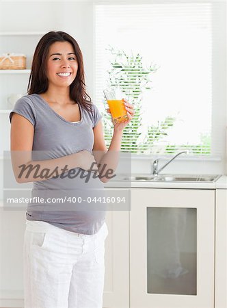 Gorgeous pregnant woman holding a glass of orange juice while standing in the kitchen