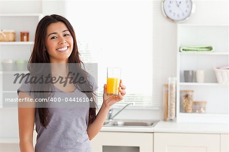Attractive woman holding a glass of orange juice while standing in the kitchen