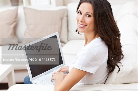 Beautiful young brunette woman at home sitting on sofa or settee using her laptop computer and smiling
