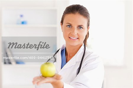 Doctor with stethoscope holding an apple looking into the camera in the surgery