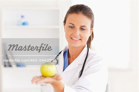 Smiling doctor with stethoscope holding an apple in the surgery