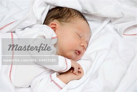 A young baby is sleeping on a white bed with a blanket.