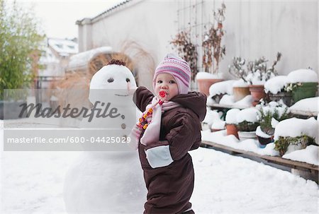 Baby Girl Playing with Snowman in Backyard