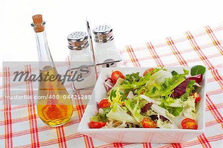 Olive oil bottle, green salad in the bowl, salt and pepper