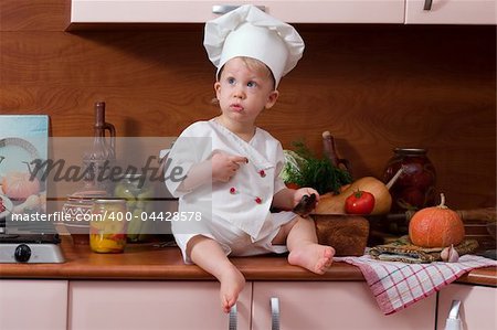 little boy in the cook costume at the kitchen sitting on the table