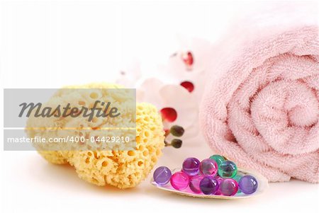 Pink rolled up towel with bath beads and natural sponge on white background