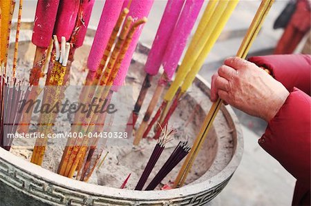 Close-up of an old woman's hands as she offers incense at a temple in China - travel and tourism.