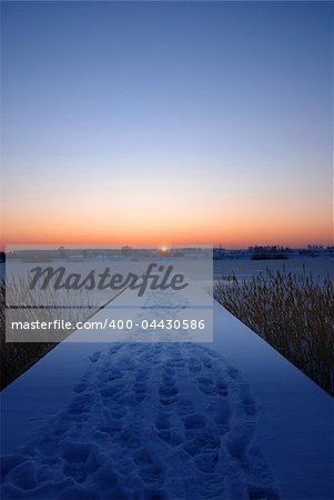 A pier by a frozen lake at sunset