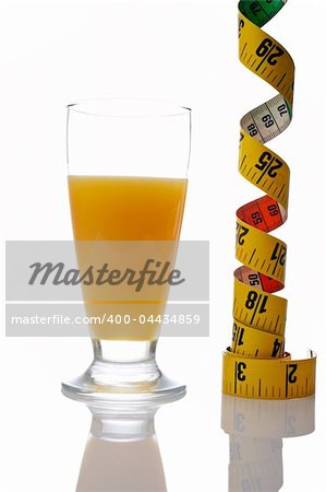 A glass of fresh orange juice and tape measure reflected on white background