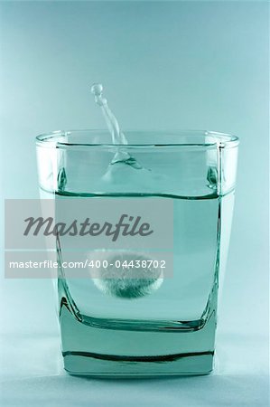 An aspirin tablet sinking in the glass with water.