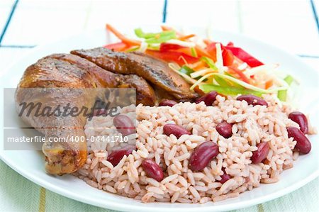 Caribbean style jerk chicken served with rice mixed with red kidney beans. Dish accompanied with vegetable salad. Shallow DOF on the rice.
