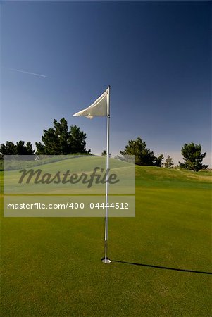 Image of a flag blowing in the wind on golfing green and deep blue sky