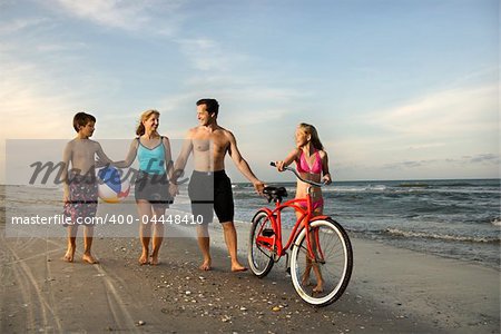 Caucasian family of four walking on beach.