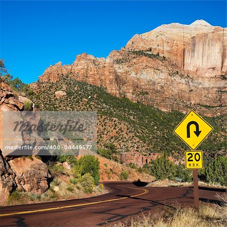 Curve caution sign on two lane road winding through rocky desert cliffs in Zion National Park, Utah.