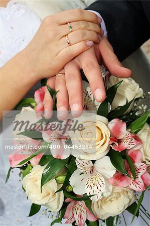 newlyweds hands with gold rings on fingers above flowers