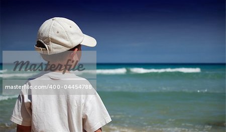 Boy in white shirt watches the waves on the beach