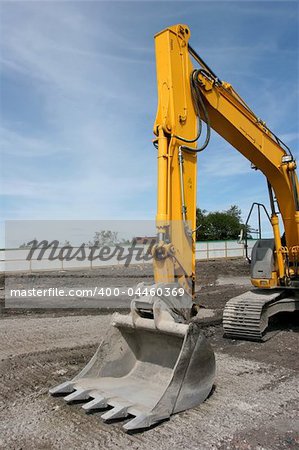 Steel excavator bucket on a yellow industrial digger, standing idle on a building site.