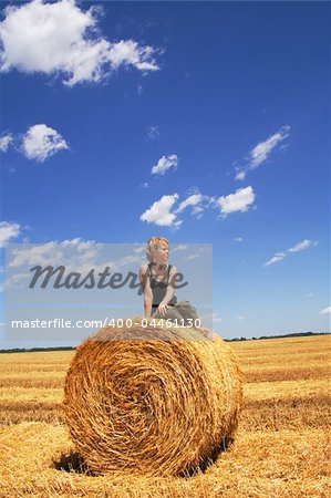 Woman sitting on a hay bale in summer stubble field under a bright vivid sky