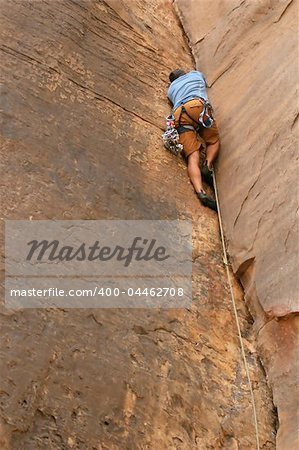 A powerful climber works his way up a crack in the cliff. He is trad climbing using cams and a rope
