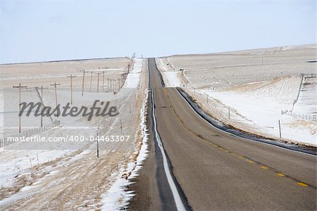 Road over rolling hill landscape with snow and power lines.
