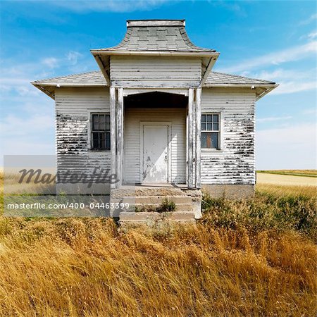 Facade of weathered abandoned building with peeling paint in grasslands.