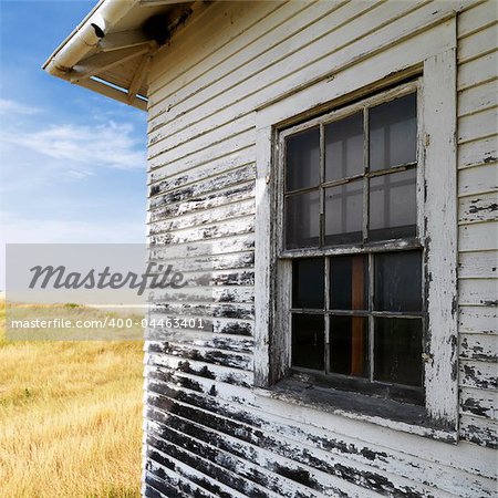 Exterior of weathered abandoned building with peeling paint and window in grassland.