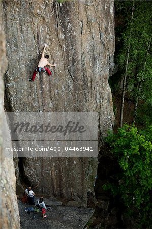 A male climber against a large rock face climbing lead.