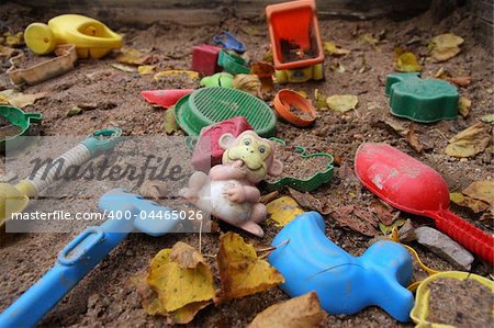 Forgotten toys in a dirty sandbox. Depressive mood.