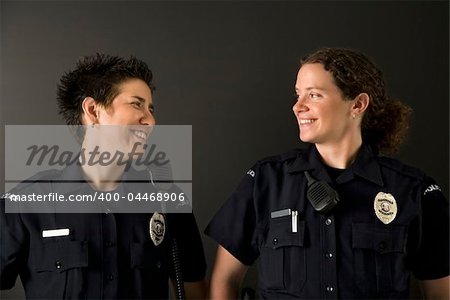 Two mid adult Caucasian policewomen standing looking at each other smiling.