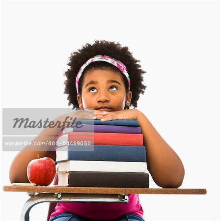 African American girl sitting in school desk with large stack of books looking bored.