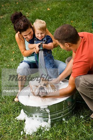 Caucasian family with toddler son giving  English Bulldog a bath outdoors.