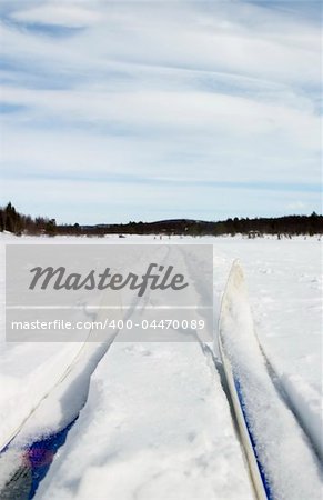 Cross country skiing trail and skis across a frozen lake.