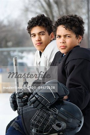 Two boys in ice hockey uniforms sitting on ice rink sidelines looking.