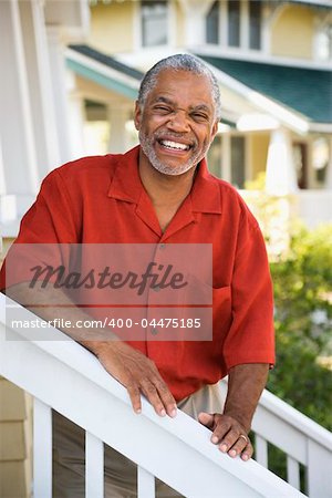 African American middle aged man smiling at viewer and leaning on stairway railing.