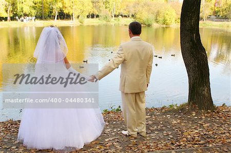 Bride and groom holding hands in autumn park before pond