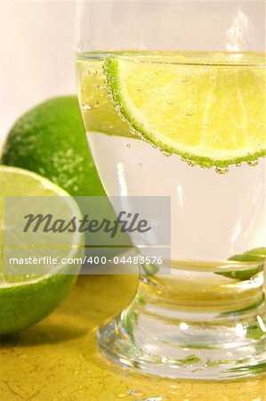 Soda with lime wedge and limes on yellow surface