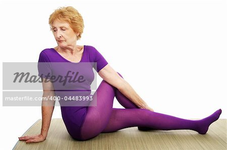 A senior woman in her seventies doing the spinal twist asana in yoga.  White background.
